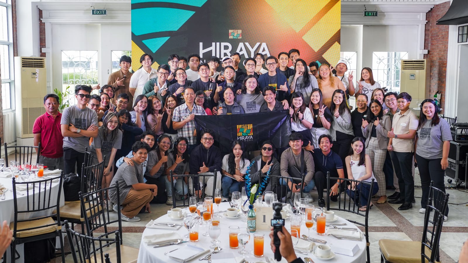 Members of the Hiraya Network Aptos community gathered around their banner at an indoor event led by The BLOKC.