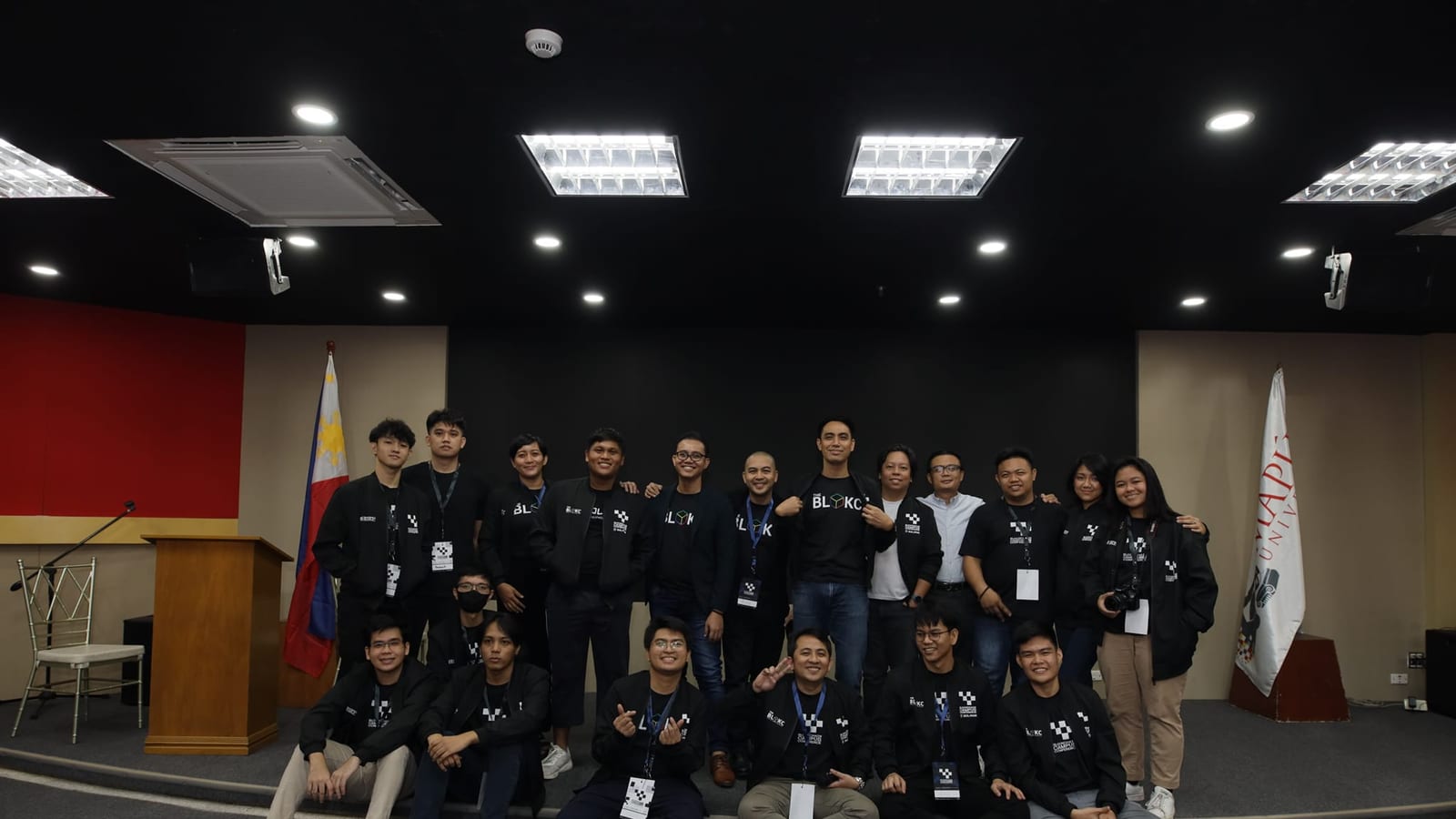 The BLOKC team and organizers pose on stage beside the Philippine flag and a Mapúa University banner at a Blockchain Campus Conference.