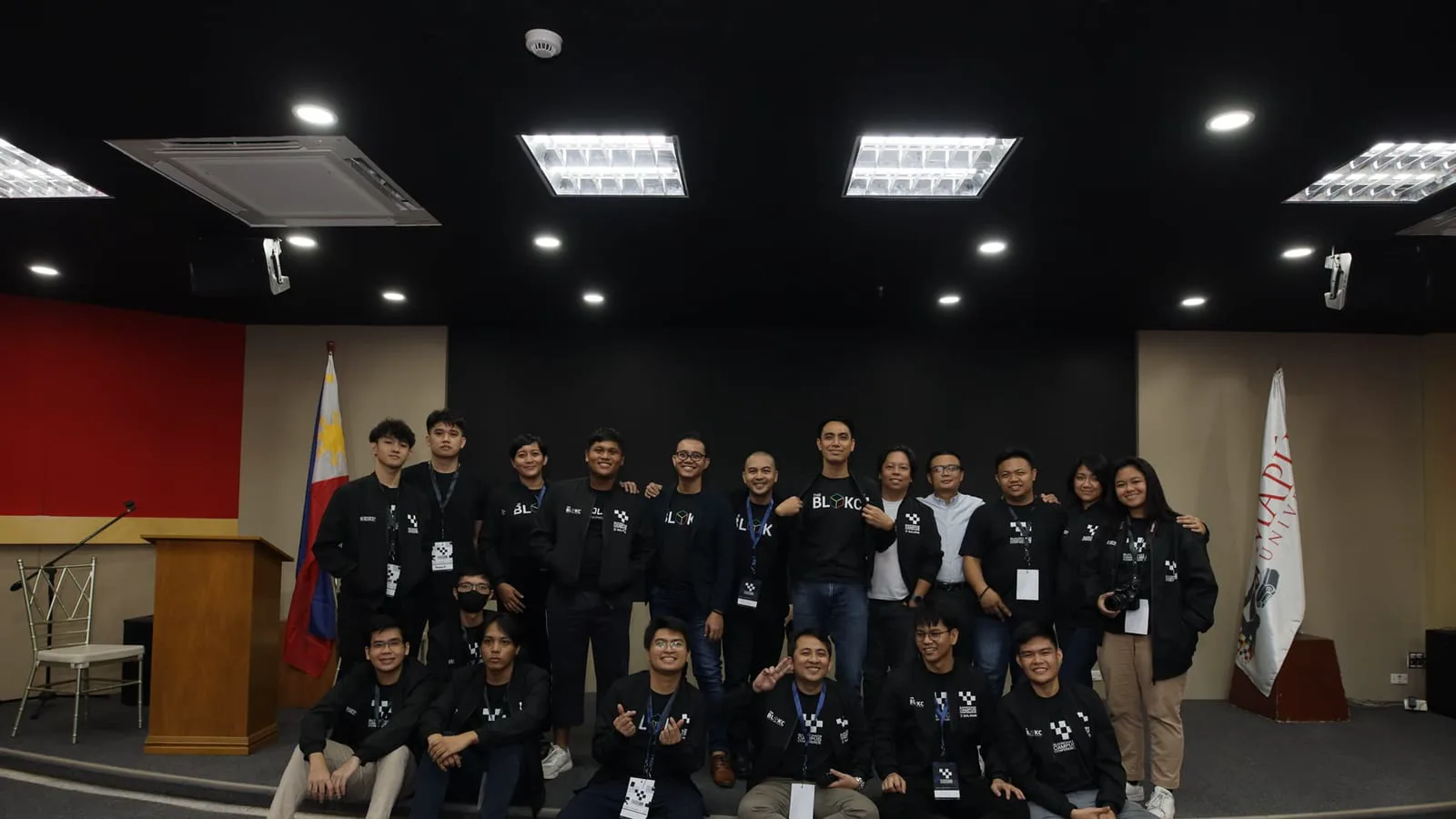 The BLOKC team and organizers pose on stage beside the Philippine flag and a Mapúa University banner at a Blockchain Campus Conference.