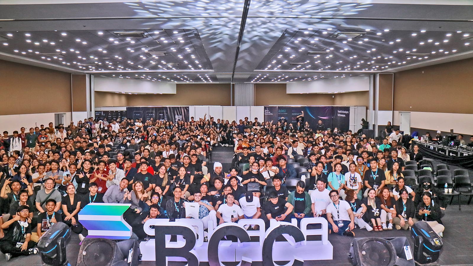 Hundreds of attendees fill a venue for a sweeping group photo behind giant BCC letters at the Blockchain Campus Conference in Davao.