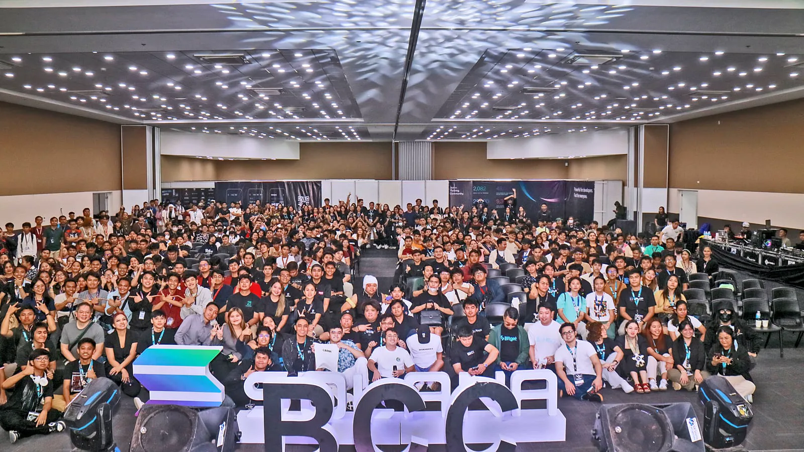 Hundreds of attendees fill a venue for a sweeping group photo behind giant BCC letters at the Blockchain Campus Conference in Davao.