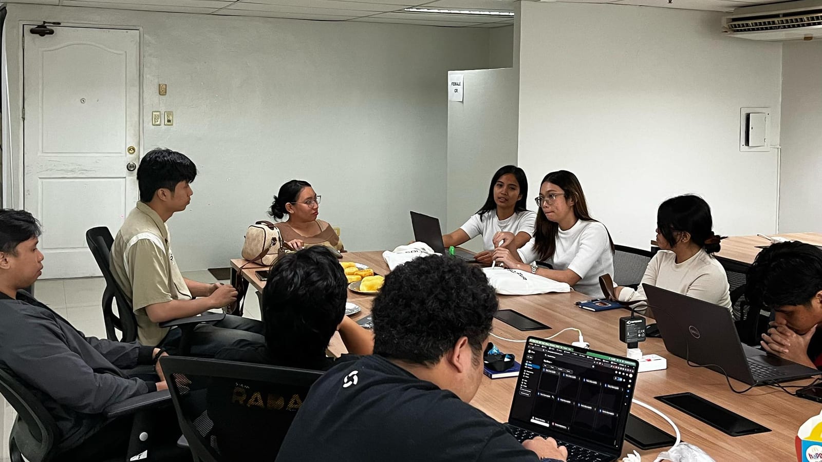 Incubation team gathered around a long conference table reviewing their startup project together with laptops open.