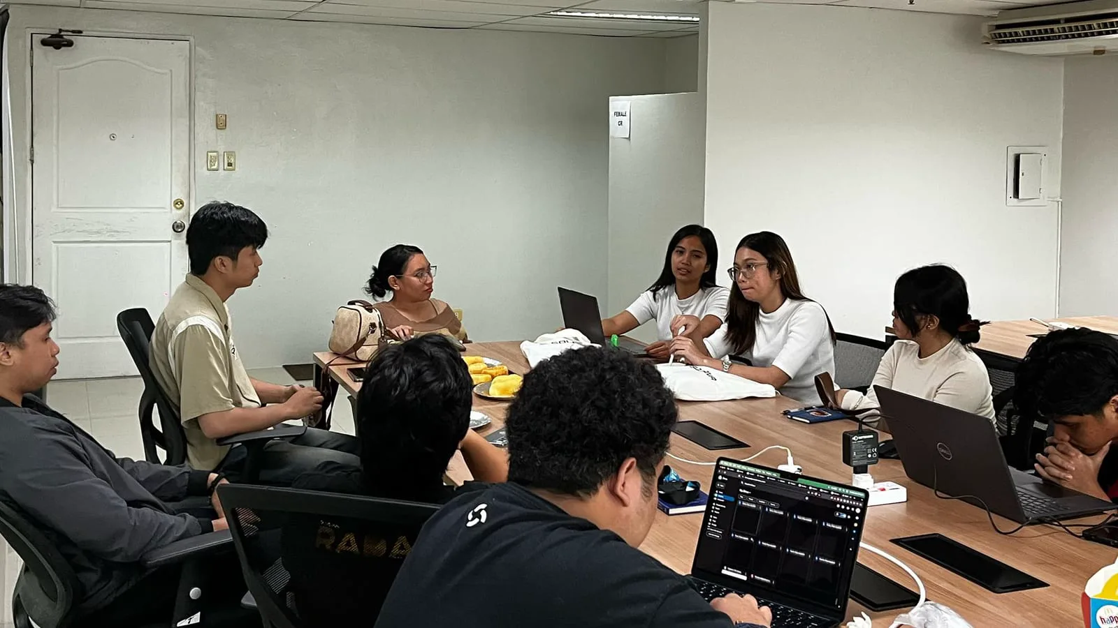 Incubation team gathered around a long conference table reviewing their startup project together with laptops open.