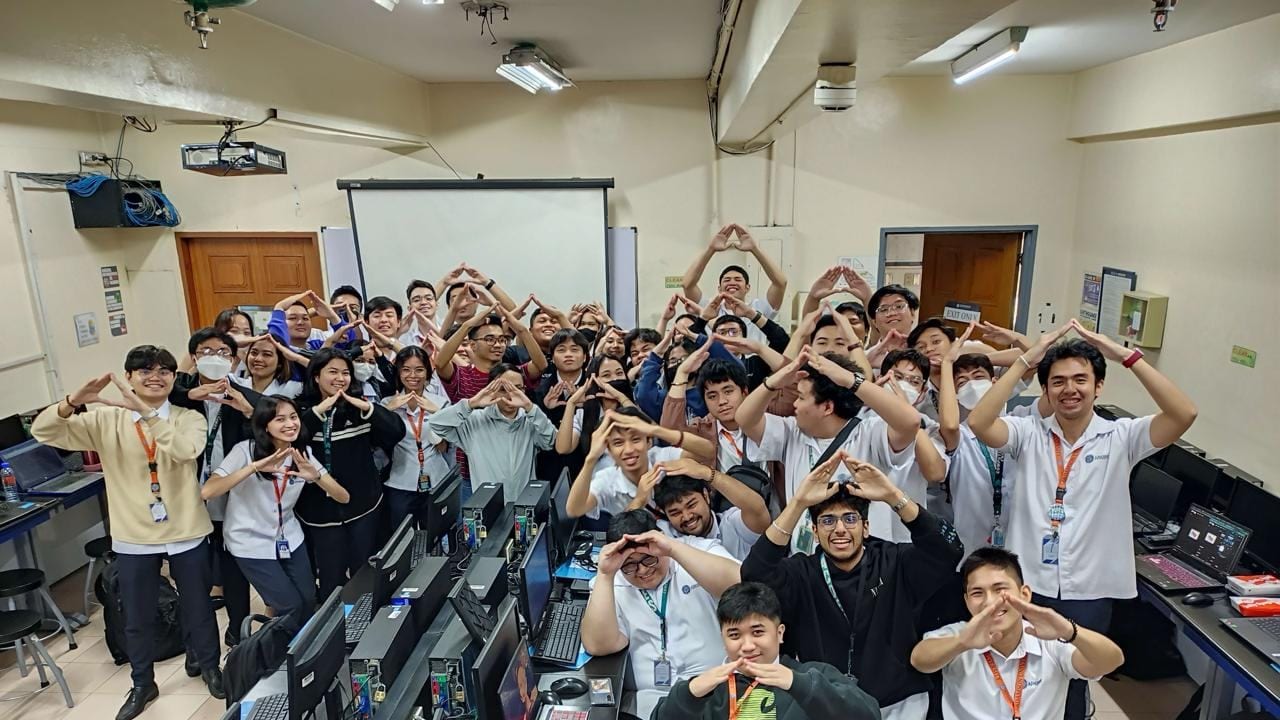 Students in a university computer lab form BLOKC hand signs together for a group photo at the end of a bootcamp.