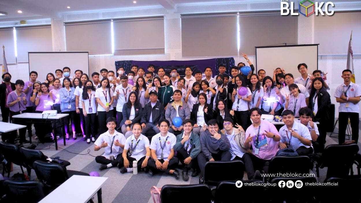 Dozens of BLOKC bootcamp participants pose together for a group photo in a purple-lit hall under the BLOKC logo.