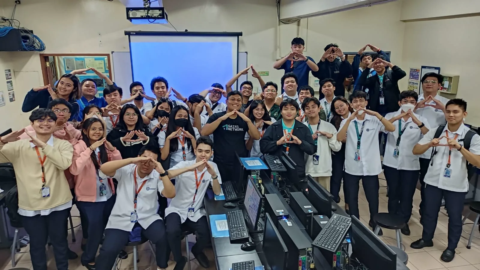 Students in a computer lab form BLOKC hand signs around a speaker wearing a Gates Network shirt at the close of a bootcamp session.