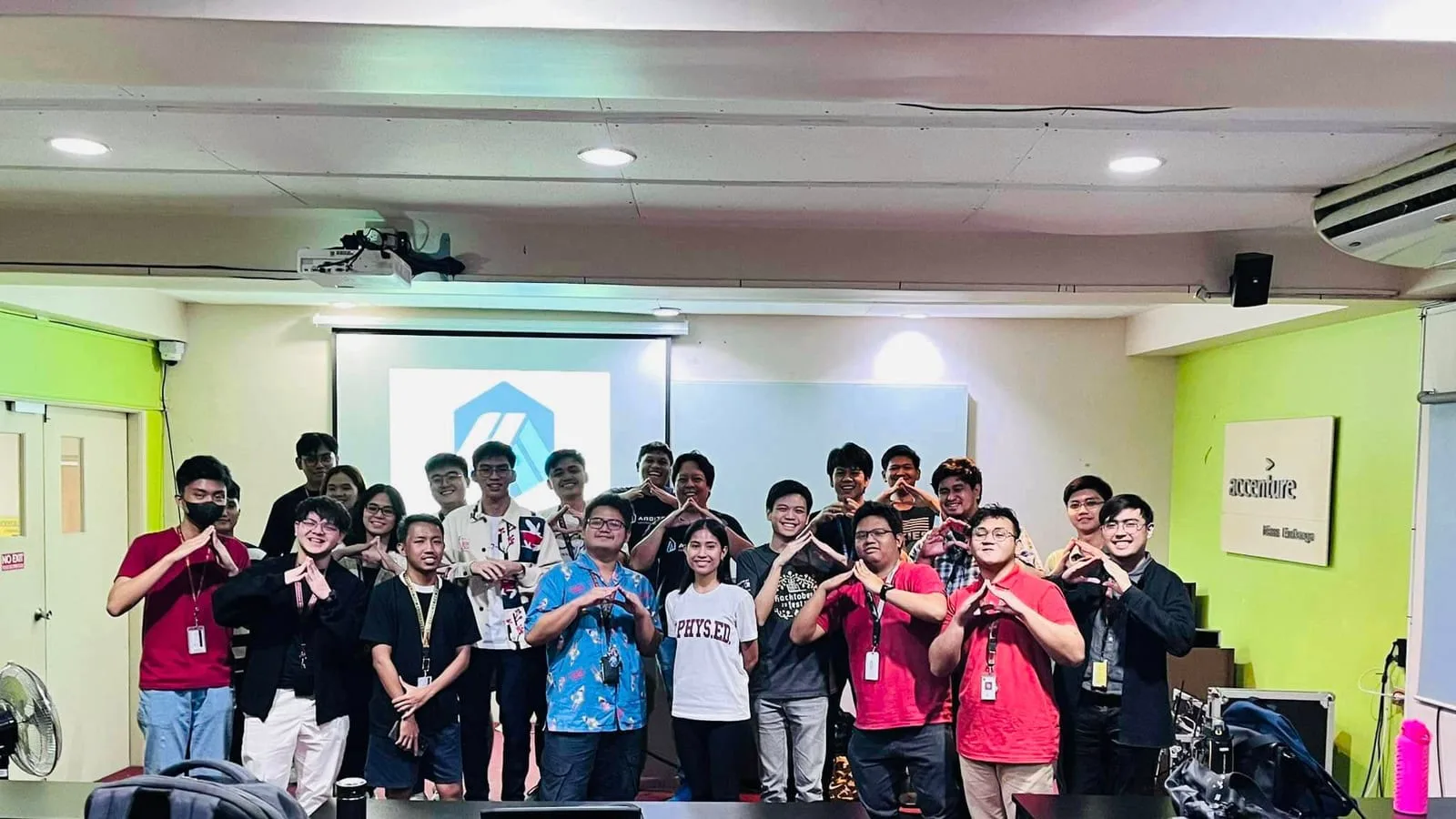 A bootcamp cohort poses with BLOKC hand signs in front of an Arbitrum logo on screen at an Accenture venue.