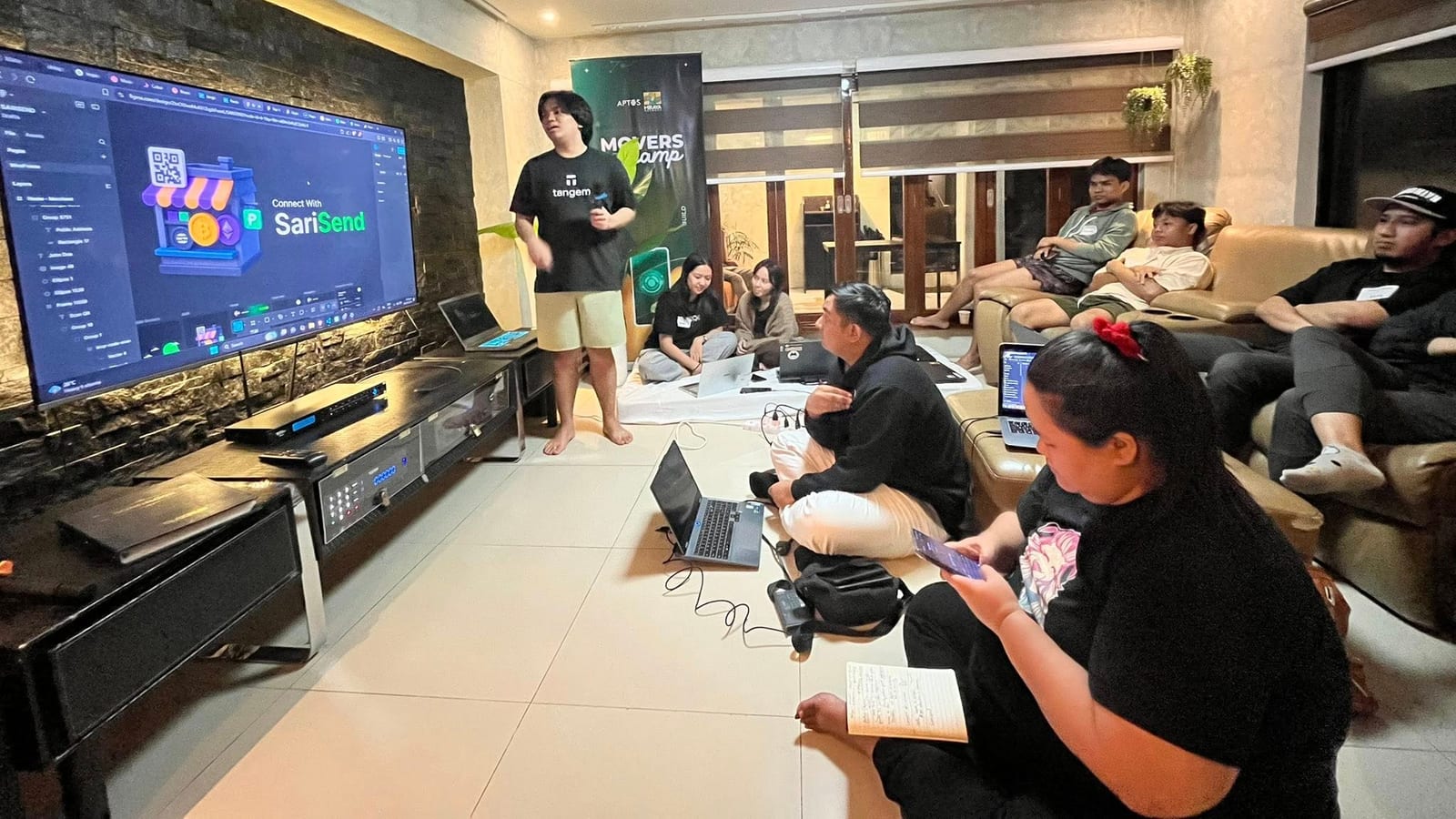A builder presents the SariSend project to a seated audience under the Movers Camp banner.