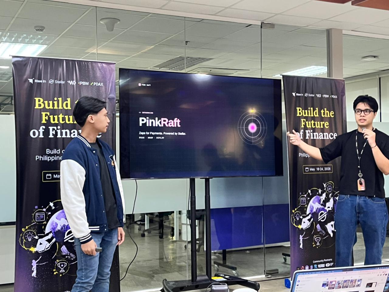 Two interns present the PinkRaft project on stage between Build the Future of Finance hackathon banners.